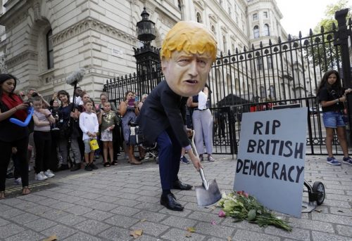A man in a giant Boris Johnson 'head' digs a grave at the foot of a pretend tombstone outside Downing Street in London, Wednesday, Aug. 28, 2019. Britain's Queen Elizabeth II has approved the U.K. government's request to suspend Parliament amid a growing crisis over Brexit. Prime Minister Boris Johnson spoke to the queen on Wednesday to request an end to the current Parliament session in September.(AP Photo/Kirsty Wigglesworth)